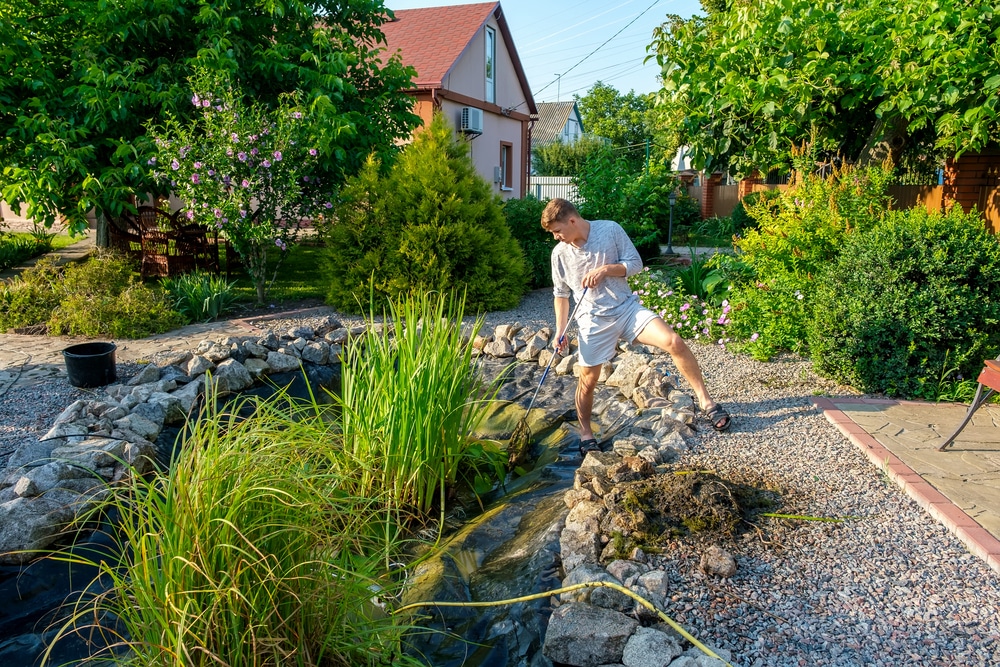 Homme qui retire l’excès de vase et de plantes aquatiques d’un étang